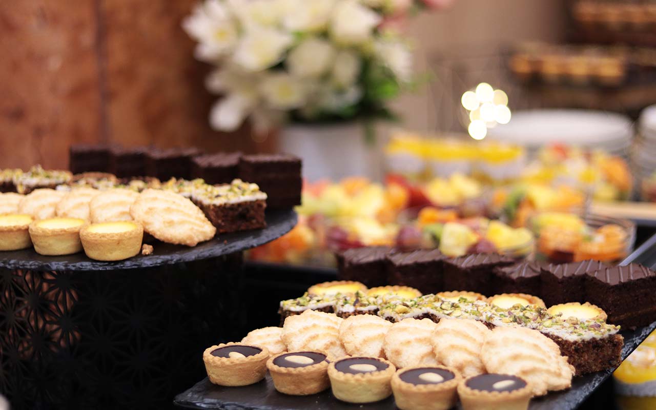 Mini sütemény válogatás, kókuszcsók, sacher, csokoládé tarte, vaníliás tarte, háttérben gyümölcssalátával